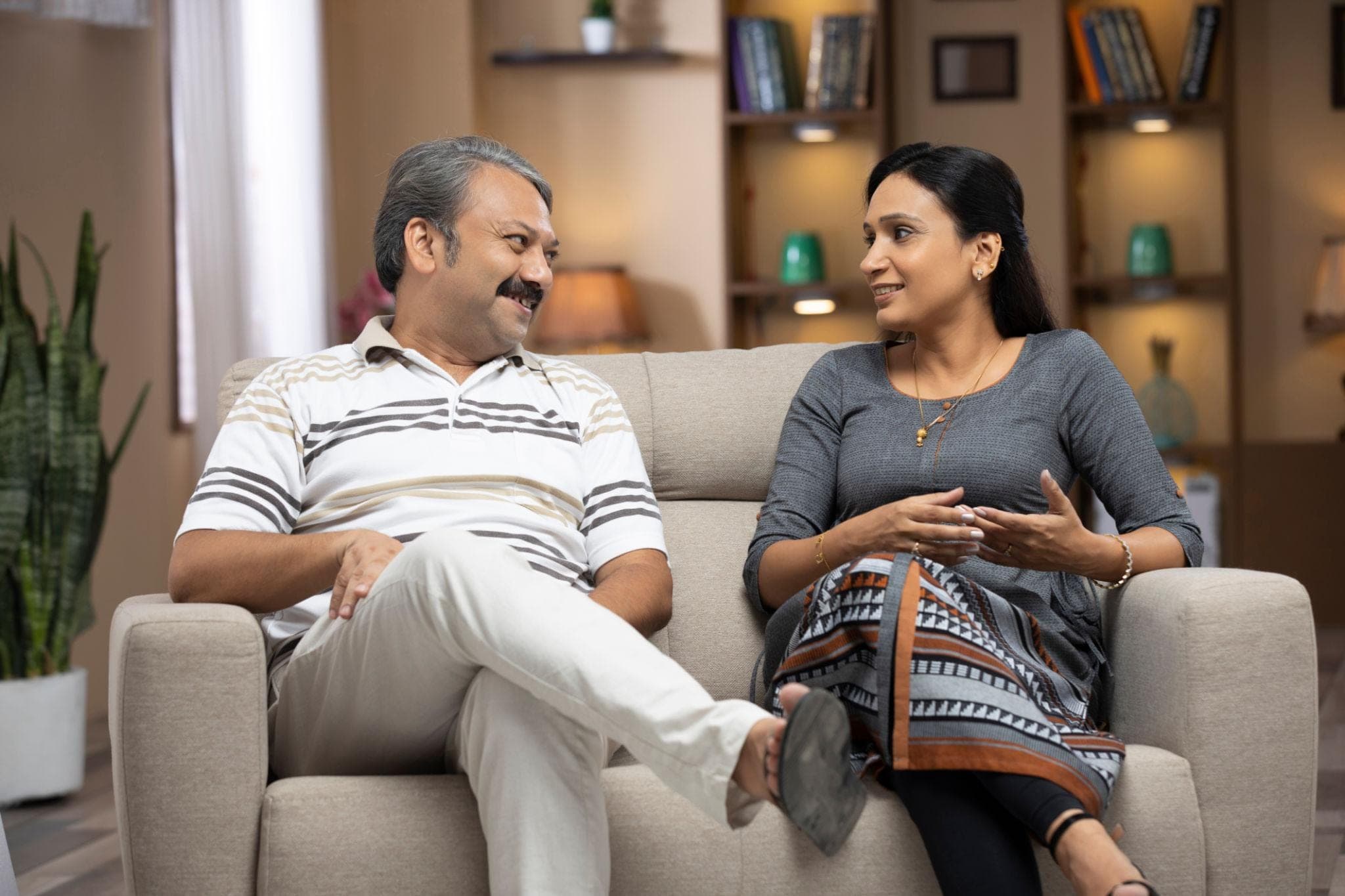 A married Indian couple sitting together in a comfortable, bright home environment, calmly talking and listening to each other., Couples Marriage Counseling